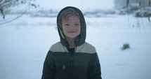 Happy, young boy smiling in cinematic slow motion snow on Christmas morning. Young kid playing in snowfall on Christmas morning.