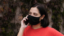 a woman talking on a cellphone outdoors wearing a mask 