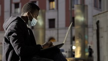 a man typing on a laptop in a city at night 