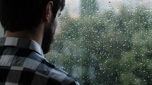 a man looking out a window through the rain 