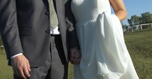 Happy newly married couple holding hands, bride and groom walking together outside after summer wedding.