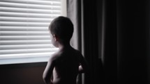 A young boy looking out a window in cinematic slow motion.