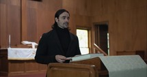 Young pastor in church with bible preaching, teaching sermon to congregation in Sunday morning worship service.