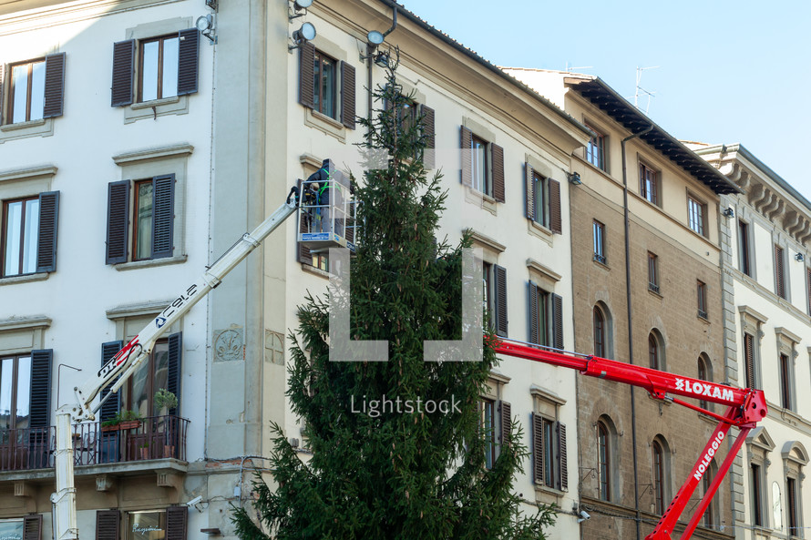 Florence, Italy - December 03, 2023: Christmas tree installation in the central square of Florence. Workers on lifting platforms mount the Christmas lights.