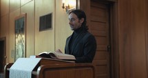 Young pastor in church with bible preaching, teaching sermon to congregation in Sunday morning worship service.