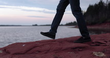 Man walks to edge of rocks in front of ocean - close up on feet