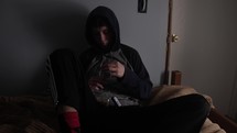 Young, sad, depressed man, teenage boy sits alone in a dark room smoking a cigarette or drugs like marijuana.