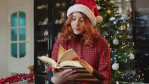 Girl reading a book against Christmas tree