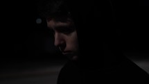 Young, sad looking and depressed young man or teenage boy walking alone at night in small town while wearing a hood in cinematic slow motion.