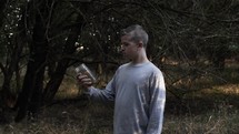 A young man holding a jar of alcohol. Unhappy, troubled teen boy holding alcohol in woods. 