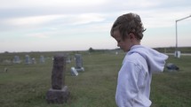 Young, sad boy in graveyard by tombstone grieving.