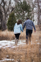 a couple walking holding hands through a snowy field 