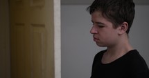 A young man, teen boy closes bedroom door. A teenager standing at his door looking depressed and unhappy closes door to his bedroom.