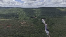 Drone flies backwards along river in forested countryside