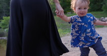 Toddler girl dances with mother on lake beach in morning sun