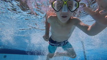 Young boy jumps in swimming pool with goggles on - summer fun