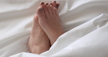Woman rubbing her feet bed sheets - close up - relaxing morning