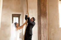 A bride and groom pull on a rope in order to ring the bell tower