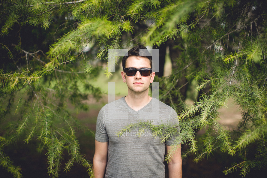 man in sunglasses standing under a tree 