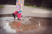 a child splashing in a puddle in rain boots