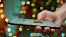 Hand navigating on the internet with blurred Christmas tree 