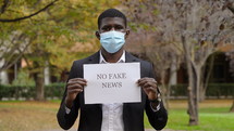 a man in a face mask holding a no fake news sign 