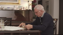 a senior man sitting at a table reading a Bible 