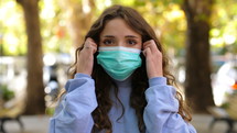 a young woman taking off a face mask outdoors 