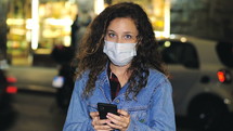a young woman texting at night wearing a face mask 