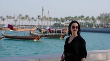 Tourist woman walking at MIA park with dhow boats behind at Doha, Qatar
