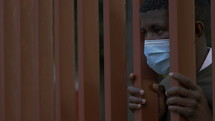 a man wearing a face mask looking through bars 