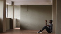 a young man sitting alone in an empty room praying 