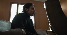 Young, emotional, anxious, and stressed man with long hair and black suit sitting in old church in worship and praying.