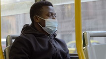 a man riding  a city bus wearing a face mask 