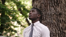 young man looking up leaning against a tree