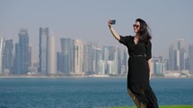 Tourist woman taking selfie at MIA park with Doha skyline behind
