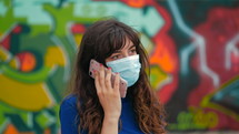 a woman talking on a cellphone standing in front of a graffiti covered wall 