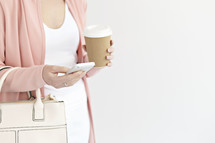 a woman with a purse holding a coffee cup and texting on a cellphone 