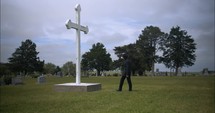 Young man kneeling in black suit looking at cross praying in worship in cinematic slow motion.