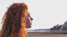 a woman standing on a shore with red hair 