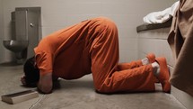 A prisoner in prison cell praying and crying next to a bible on his knees.