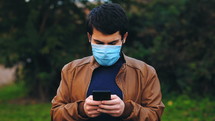 a man in a face mask texting outdoors 