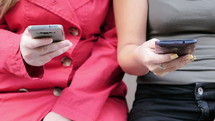 Two women texting on their cell phones.