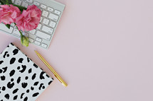 pink carnations, keyboard, pen, and spotted notebook 