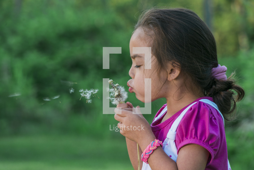 a girl blowing dandelion seeds