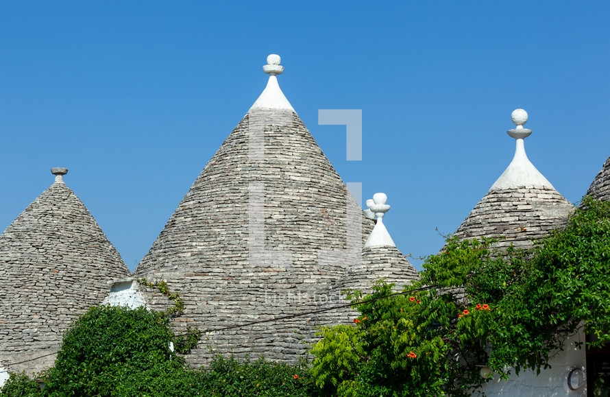 Traditional conical rooftops of trulli houses are made of piled stone slabs and decorated with white pinnacles against a blue sky