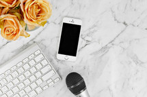 cellphone, microphone, computer keyboard, and yellow roses on a marbled background 