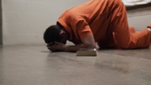 A prisoner on his knees in prison cell crying and praying next to a bible.