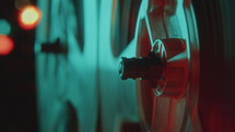 Close-up view of spinning reels of analog reel-to-reel tape recorder playing music in dark room with neon illumination and bokeh lights in defocused background
