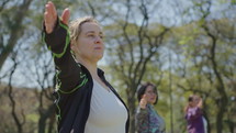 Mature woman in sportswear standing with arms outstretched and turning head, doing warrior pose on outdoor yoga practice in the park. Selective focus shot